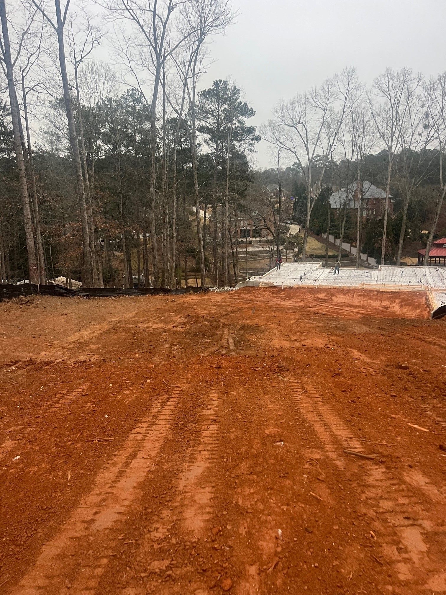 A dirt road with trees in the background and a house in the distance.