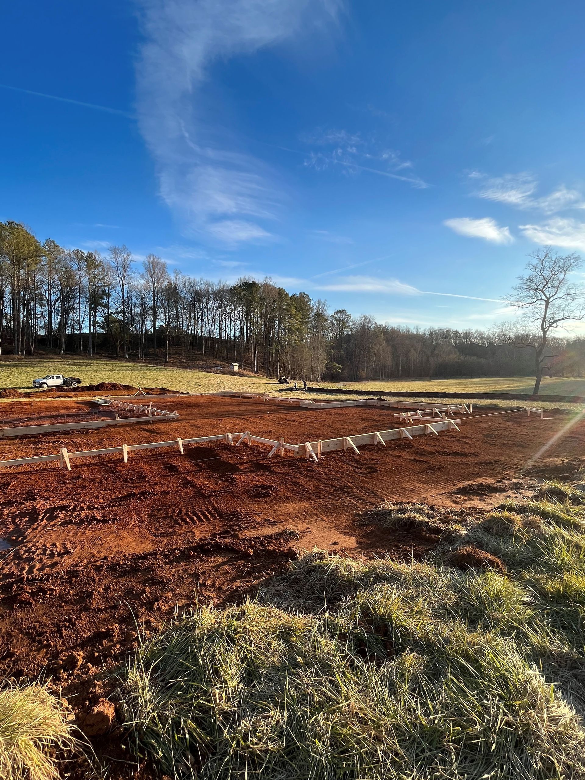A field of dirt and grass with trees in the background on a sunny day.