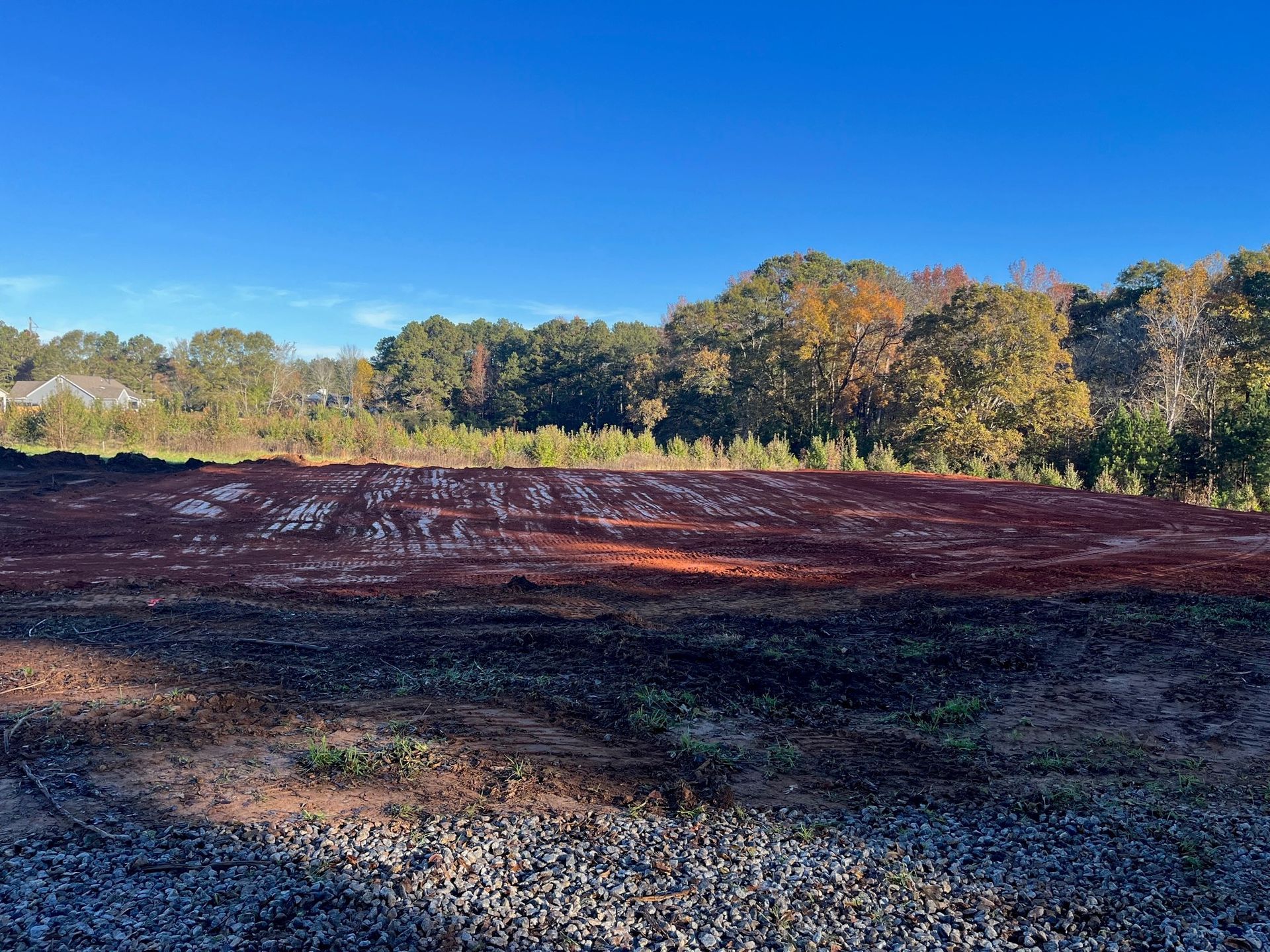 A large dirt field with trees in the background on a sunny day.
