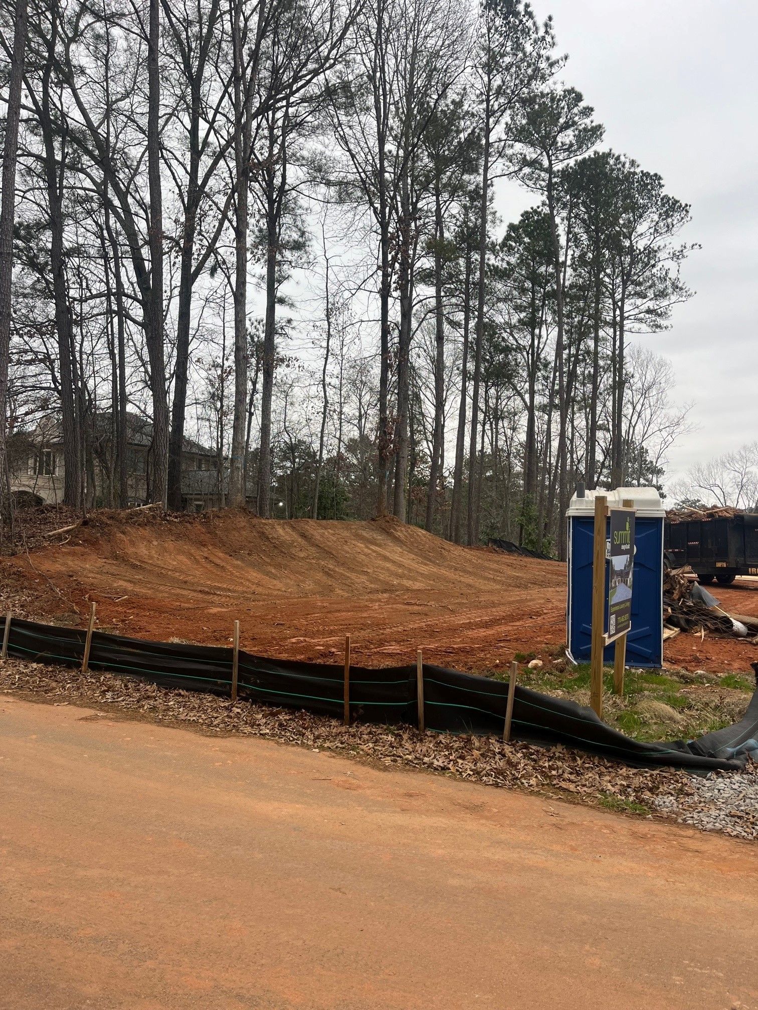 A dirt road leading to a construction site with trees in the background.