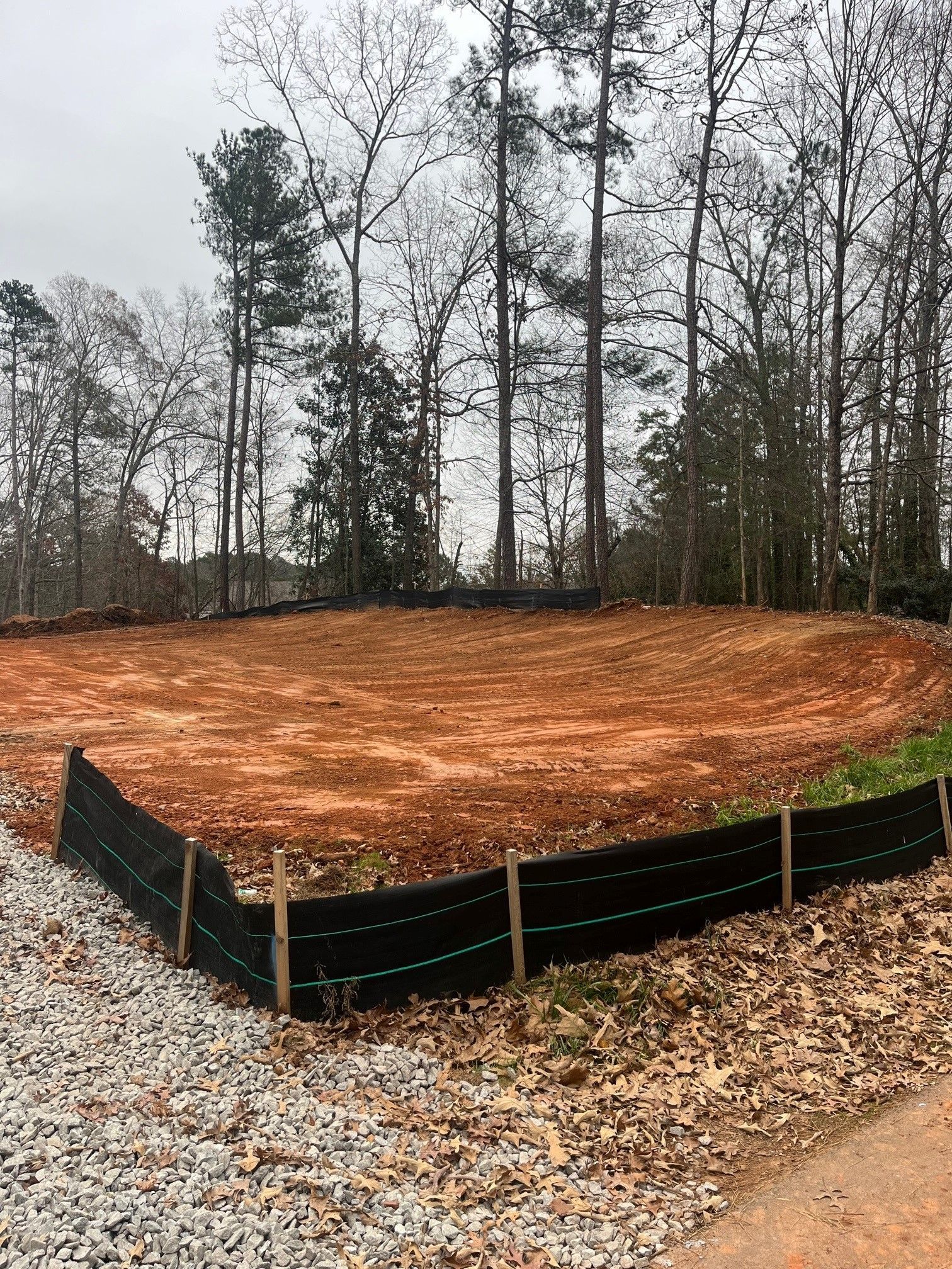 A dirt field with a black fence around it and trees in the background.