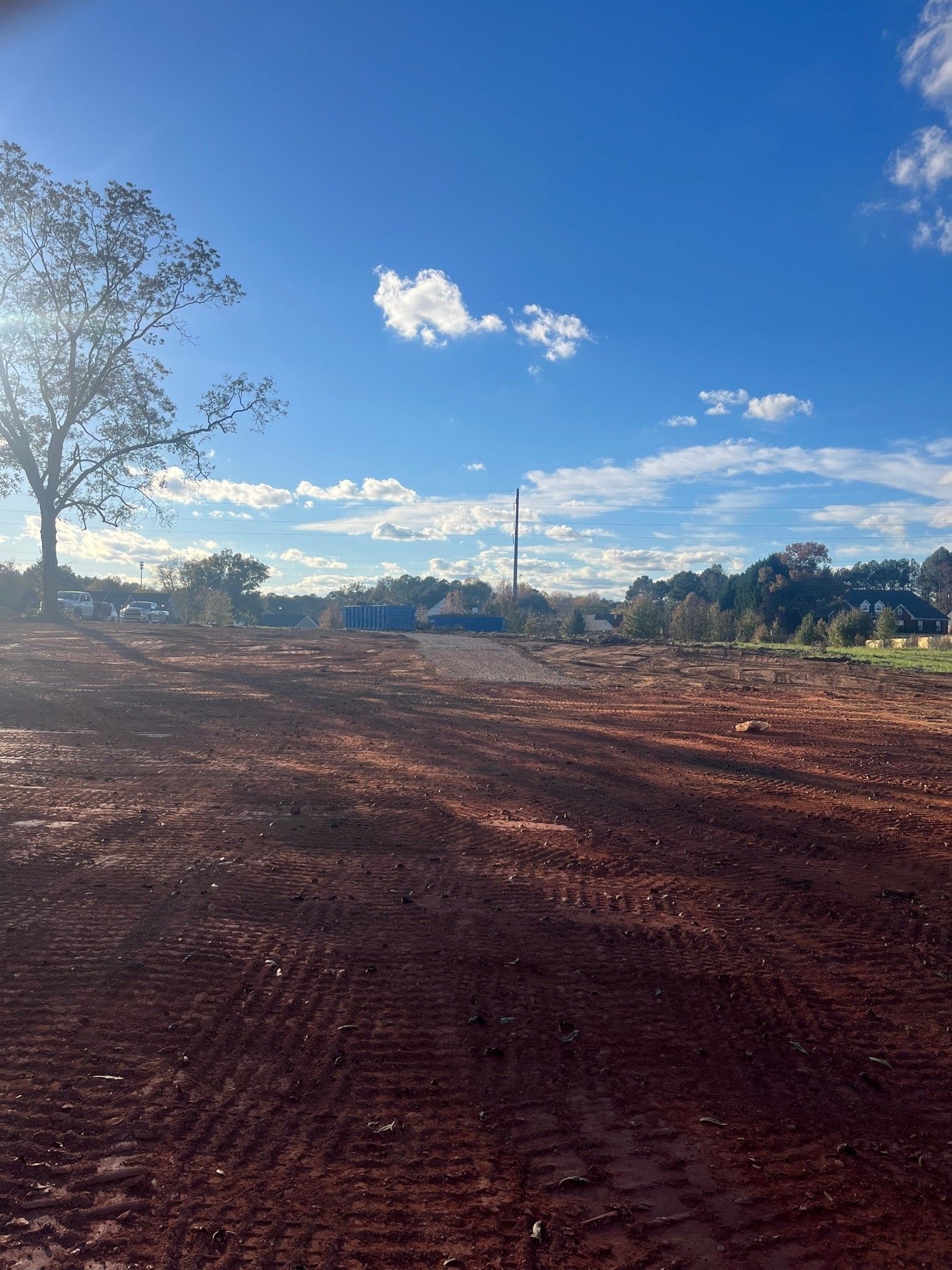 A dirt field with a tree in the background and a blue sky with clouds