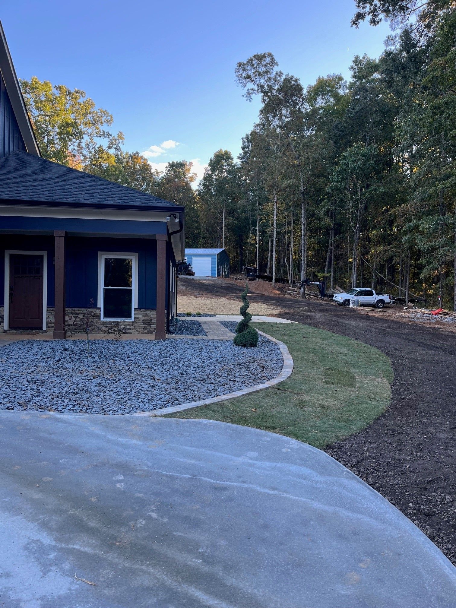A blue house with a driveway leading to it is surrounded by trees.