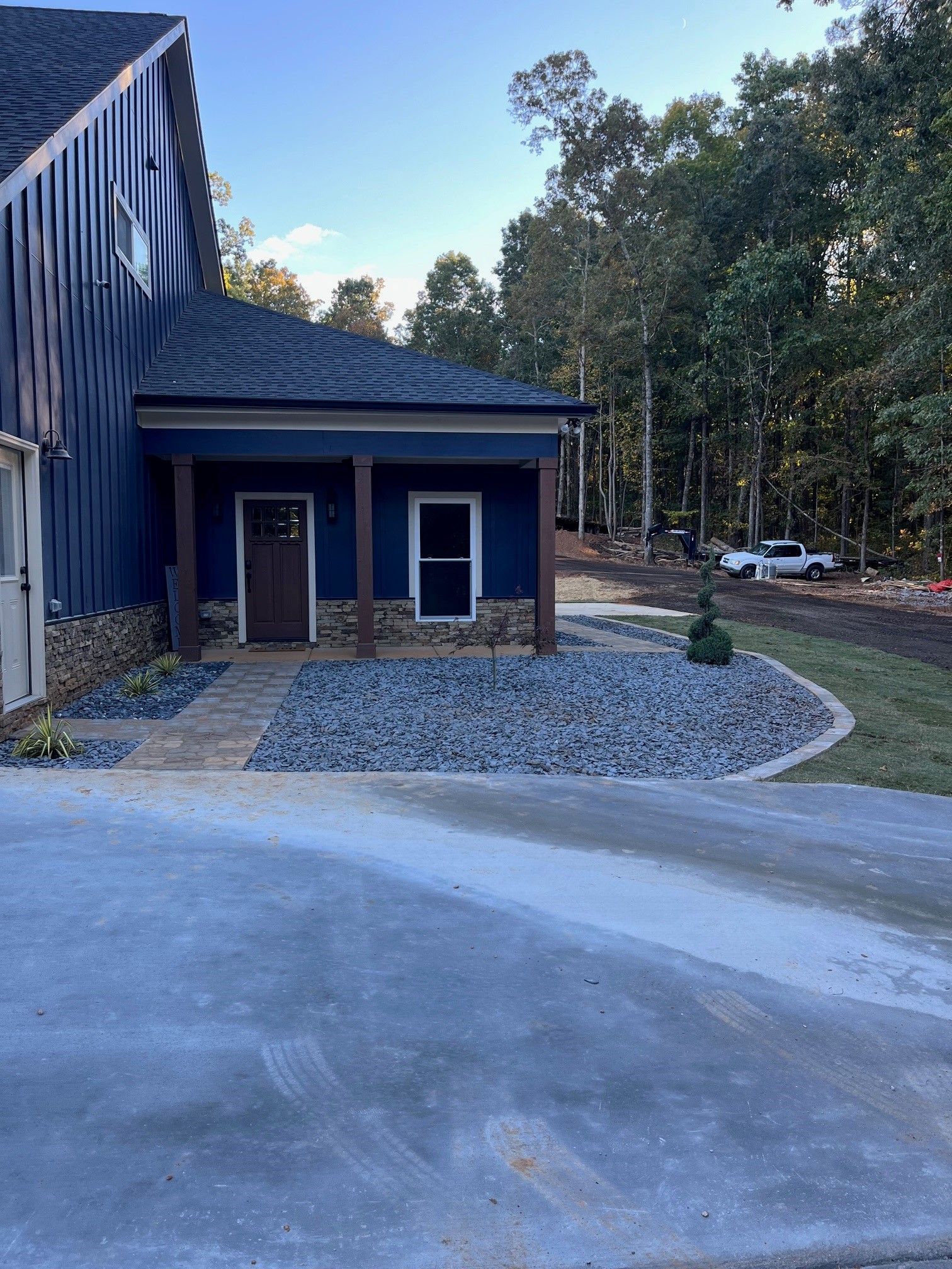 A blue house with a driveway in front of it and trees in the background.