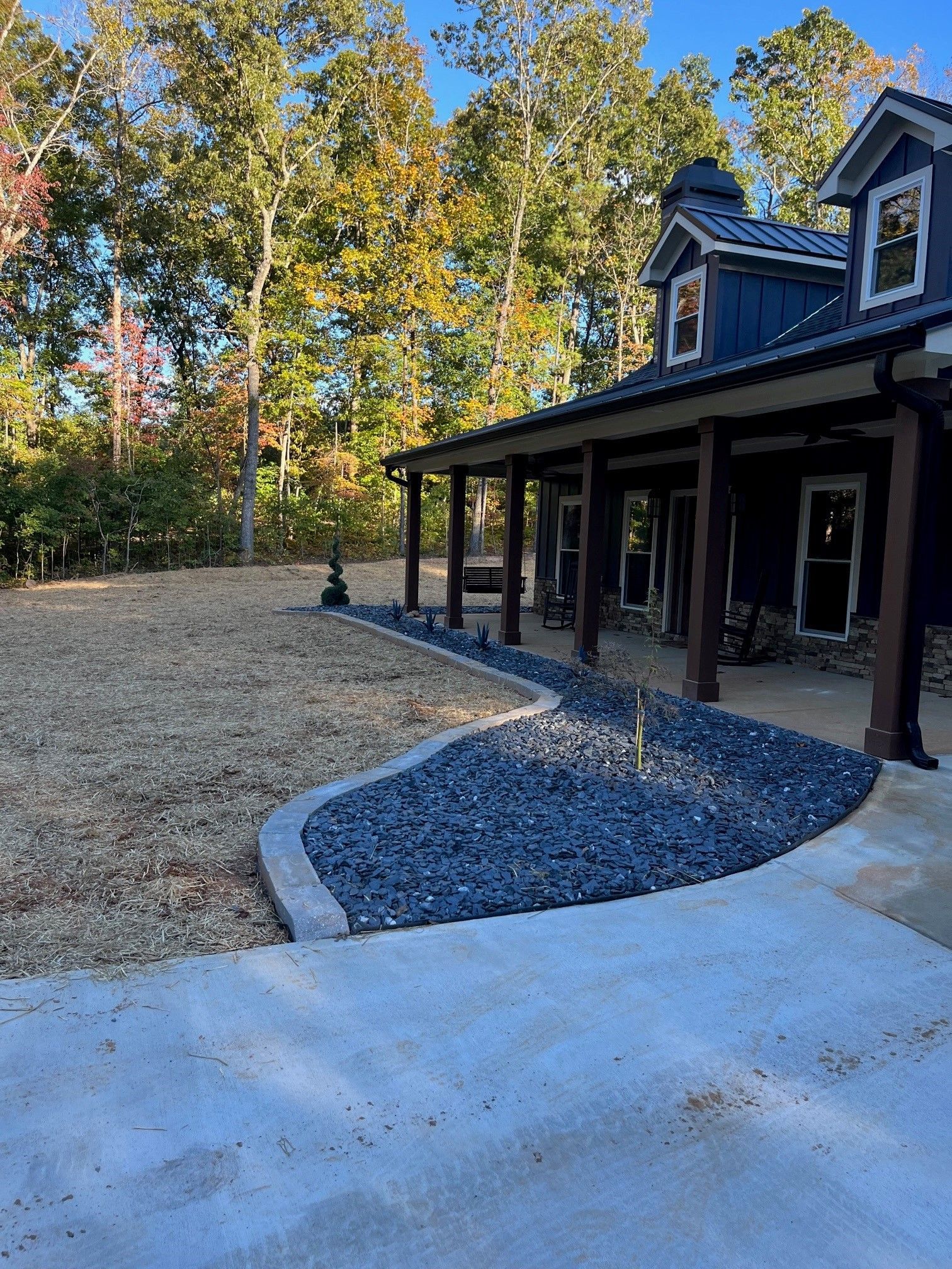 A house with a porch and a driveway in front of it surrounded by trees.