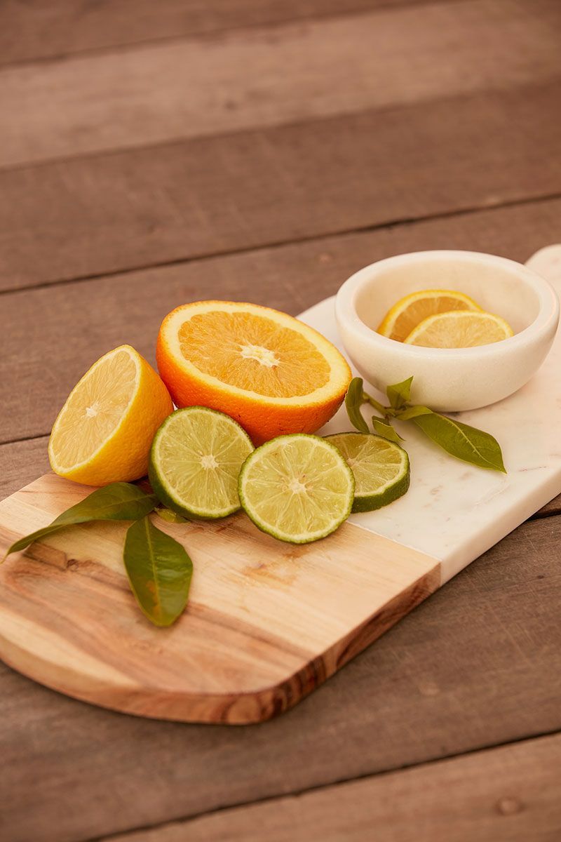 Citrus fruits (orange, lemon, and lime) arranged on a wooden cutting board, with lemon slices in a small bowl.