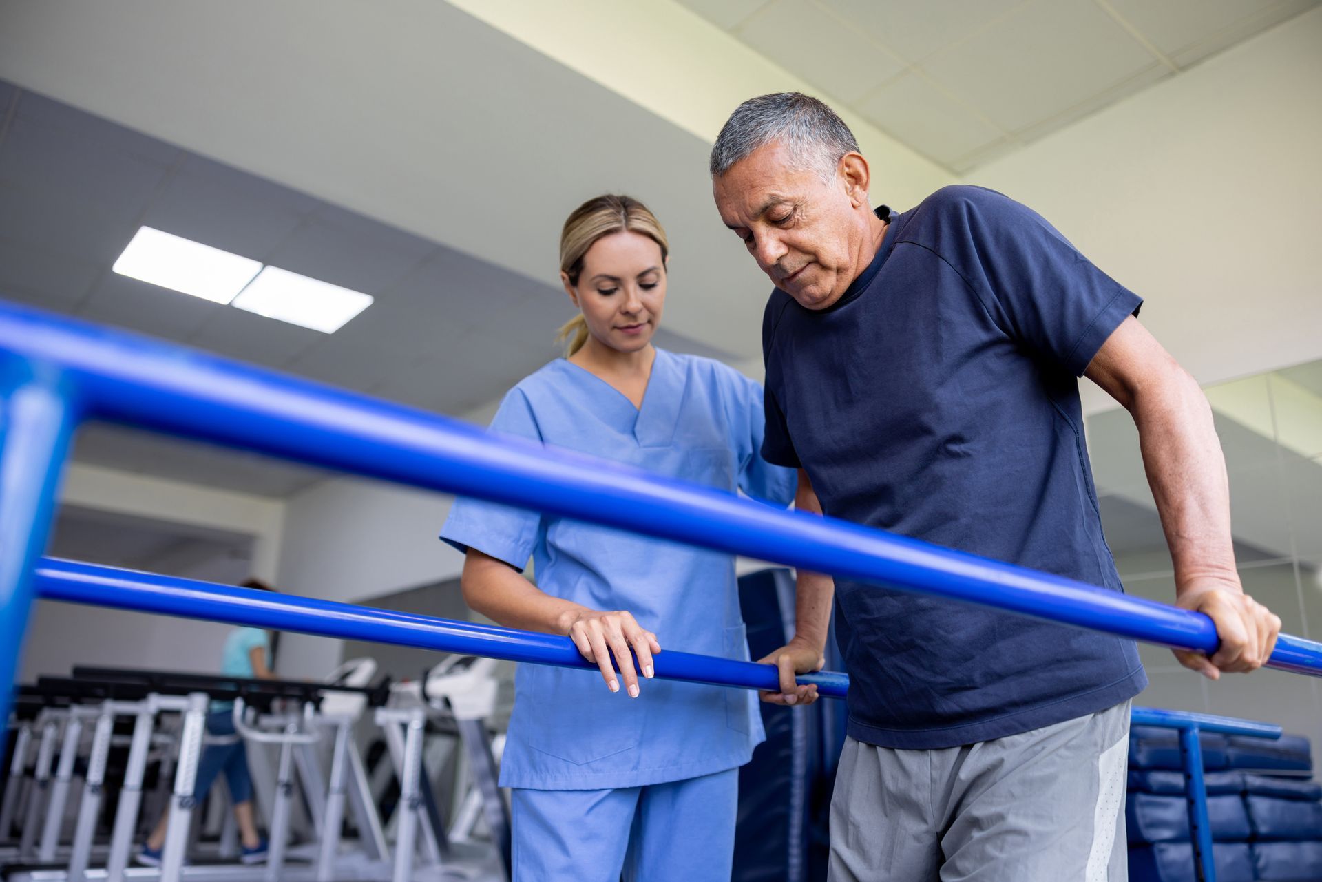 A man doing physical therapy and walking on bars with the assistance of his physical therapist. A man doing physical therapy and walking on bars with the assistance of his physical therapist.