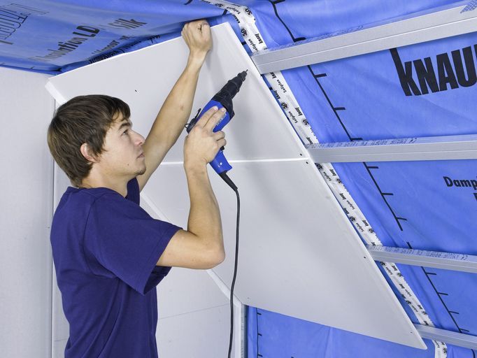 Un uomo con una camicia blu sta usando uno strumento Knauf
