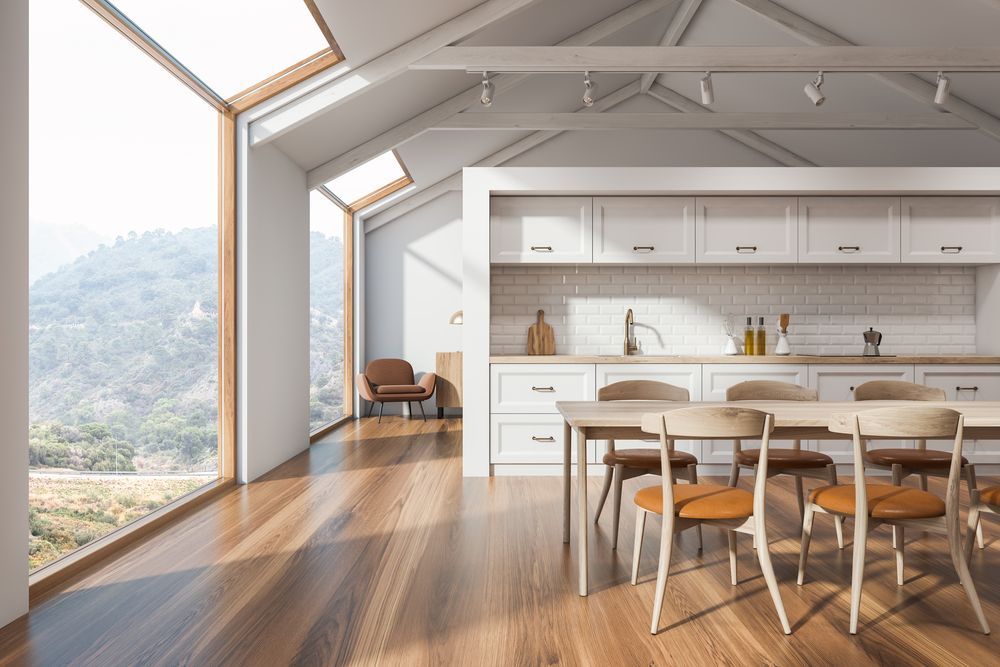 Bright modern kitchen and dining area with wood floors, white cabinets, and large windows overlooking mountains