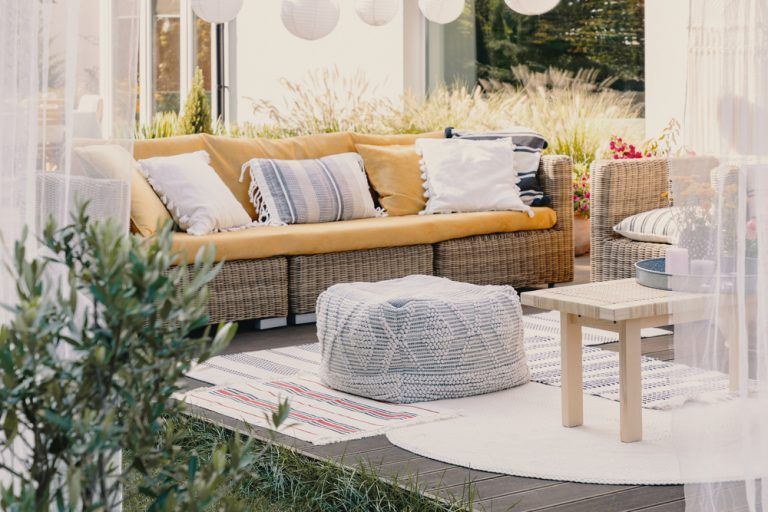 Cozy outdoor patio with wicker sofa, cushions, round chair, and small table in soft sunlight
