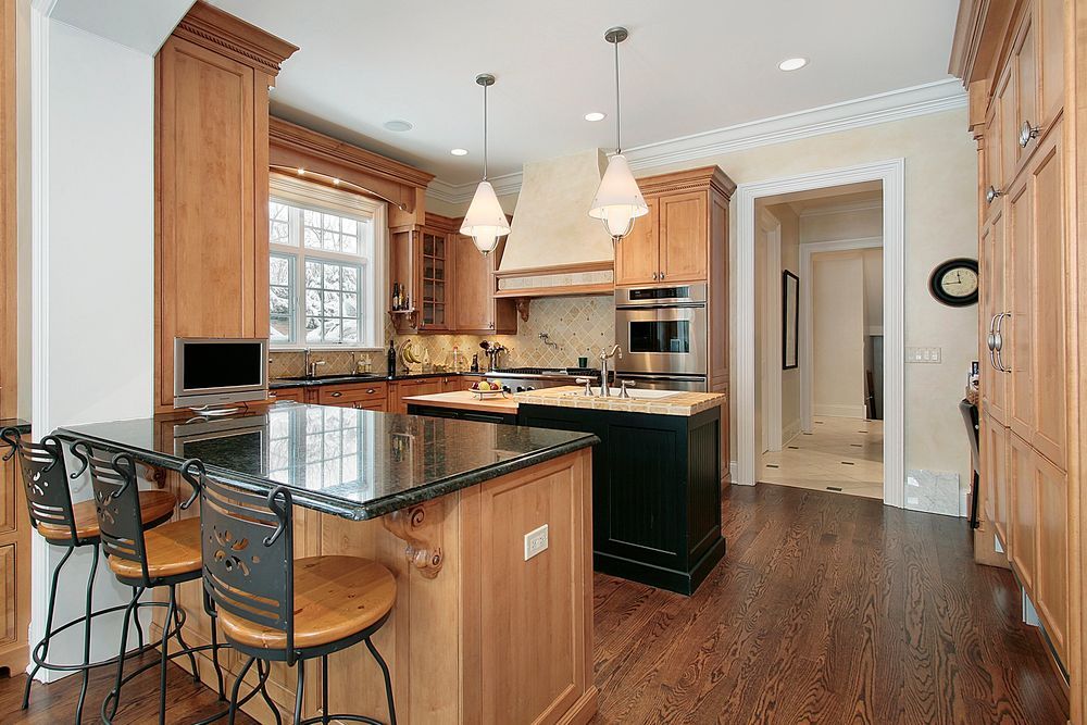 Spacious kitchen with dark granite island, wood cabinets, pendant lights, and hardwood floors