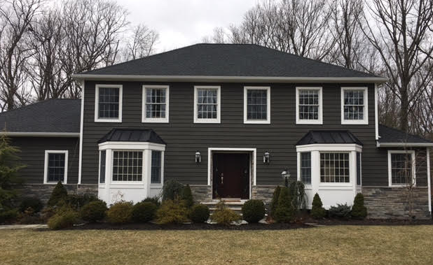 Front view of a dark gray two-story house with white trim and bay windows, surrounded by leafless trees.