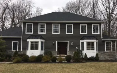Large dark-gray suburban house with white trim, a central entrance, and leafless trees in front