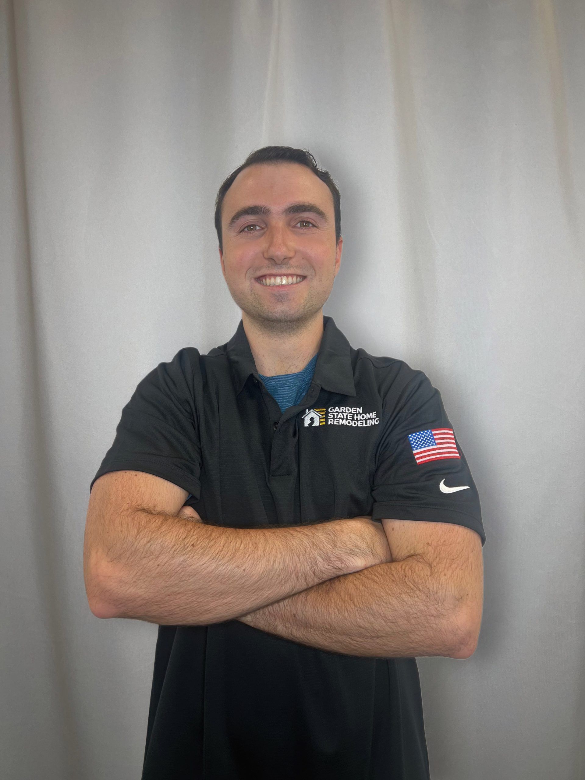 Smiling person in a black polo shirt with arms crossed against a light gray backdrop.