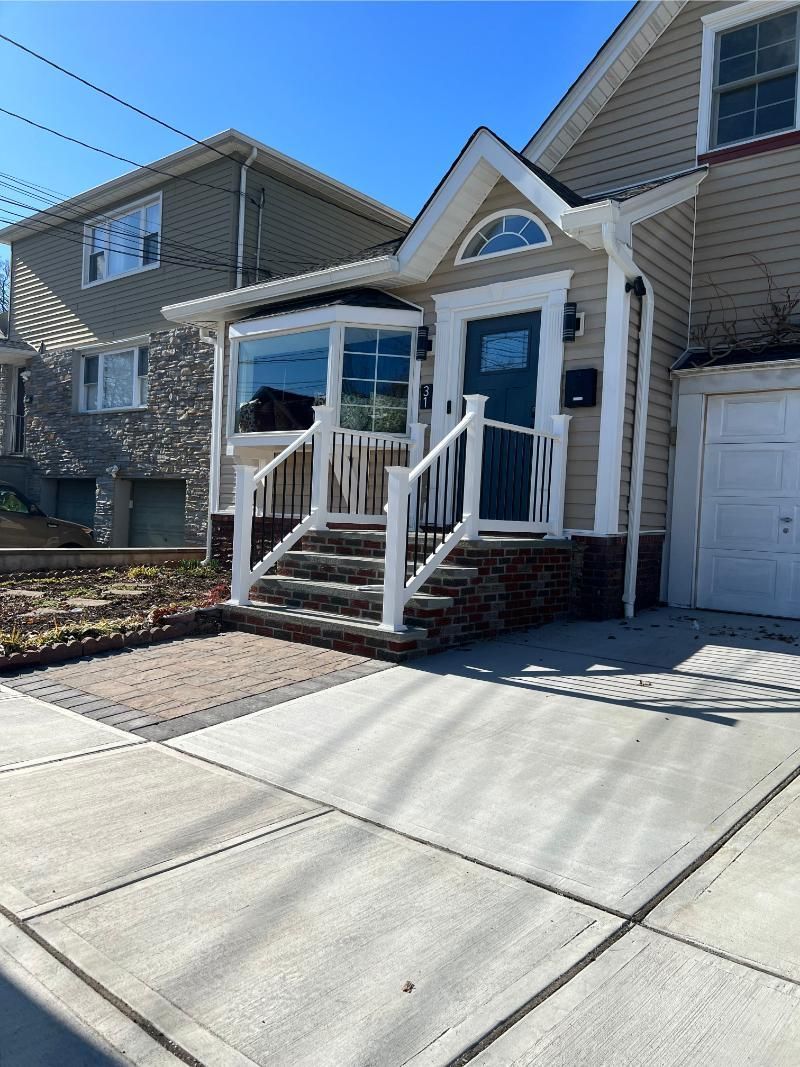 Front porch with blue door, white railings, steps, and a concrete driveway beside a house