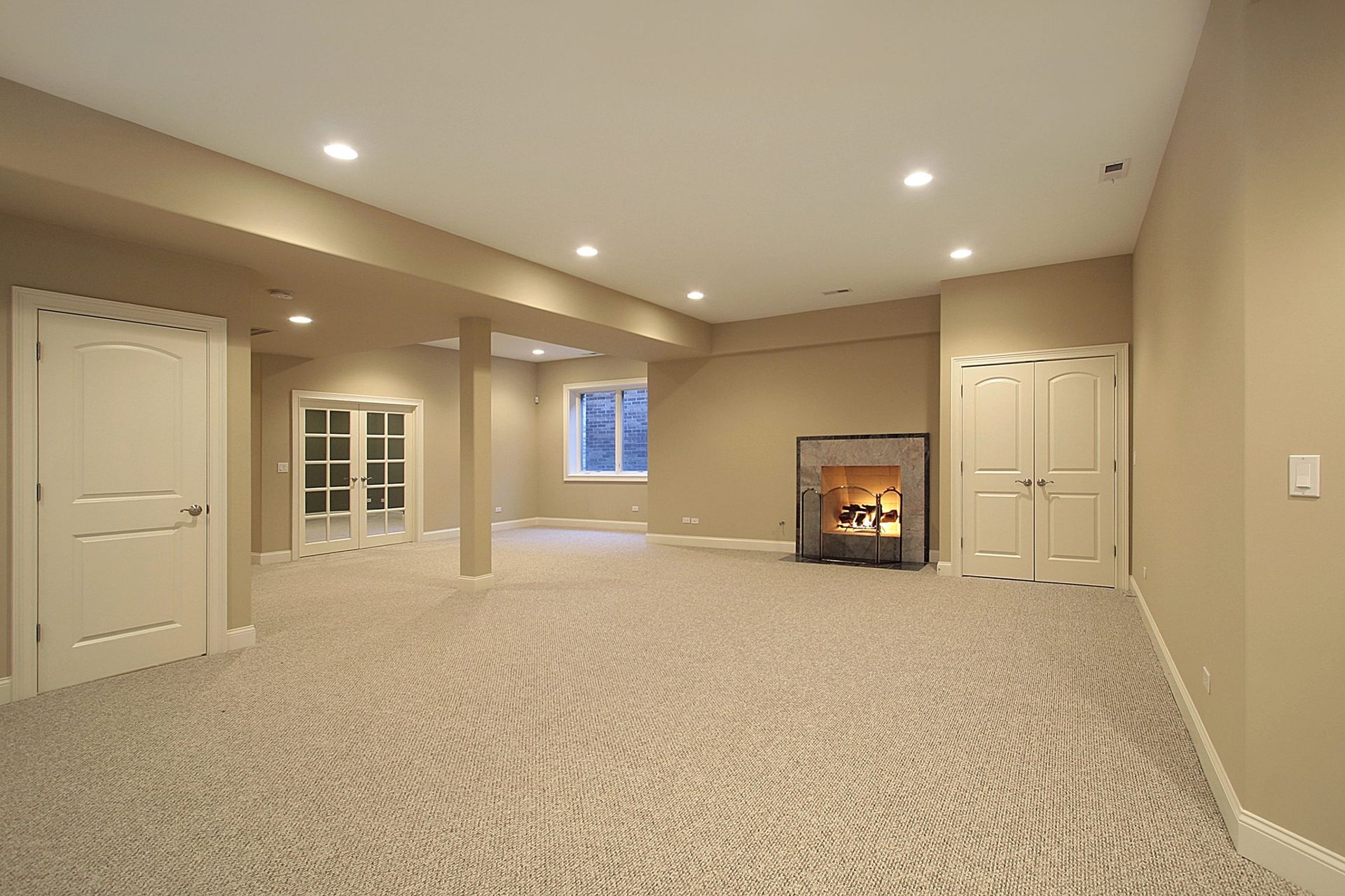 Spacious beige finished basement with carpet, recessed lights, fireplace, and windowed double doors.