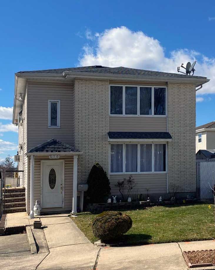 Two-story beige house with a front lawn, walkway, and blue sky with clouds
