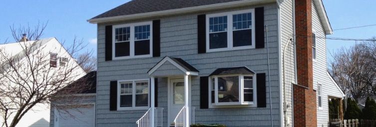 Gray two-story house with white trim, dark shutters, and a small front porch in winter.