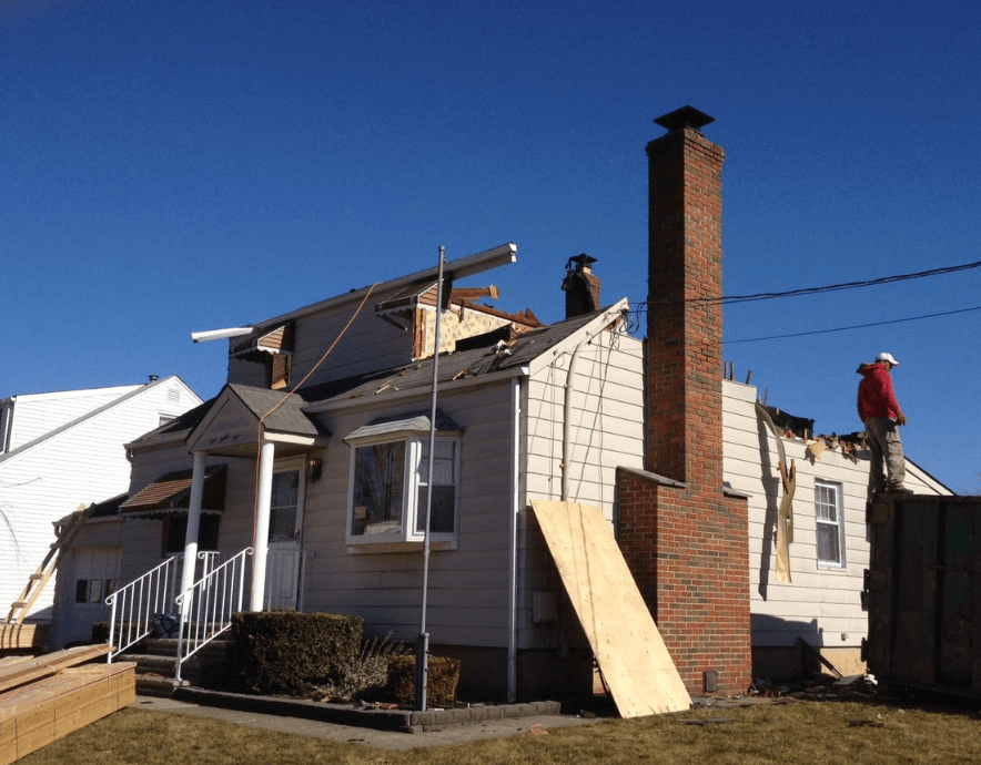 House under repair with workers on the roof, chimney, and boards leaning against the siding.