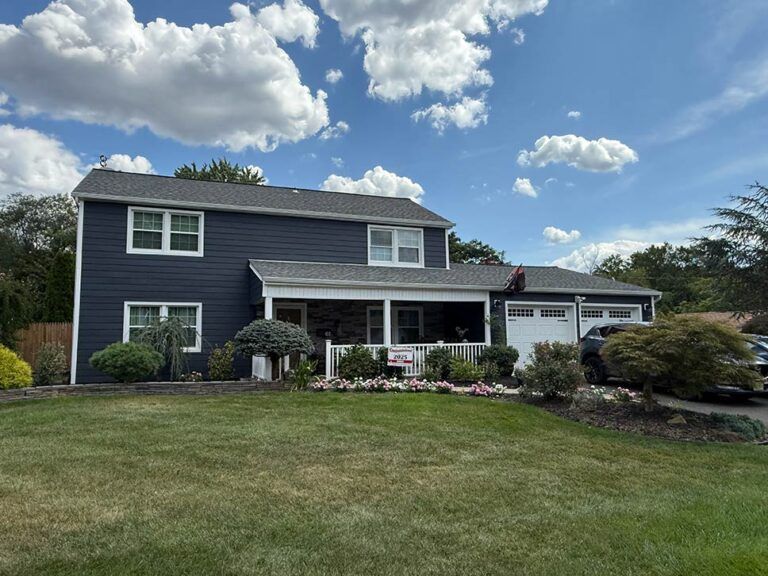 Suburban house with dark blue siding, white trim, front porch, and a large lawn under a cloudy sky