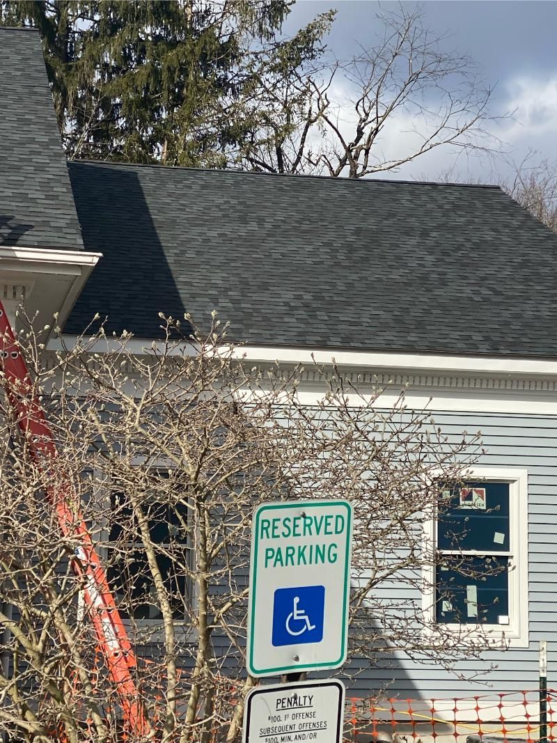 Reserved parking sign with wheelchair symbol beside a house with dark roof and white siding.