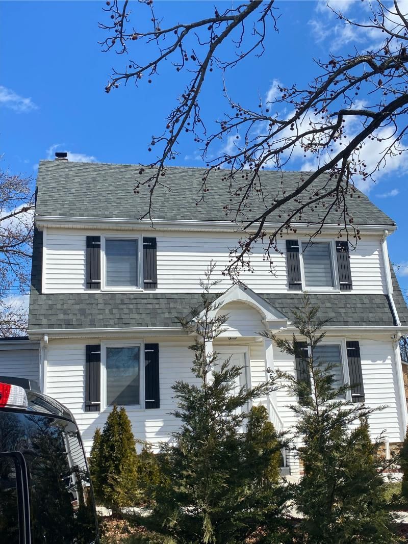White two-story house with blue shutters and a small porch under a bright blue sky