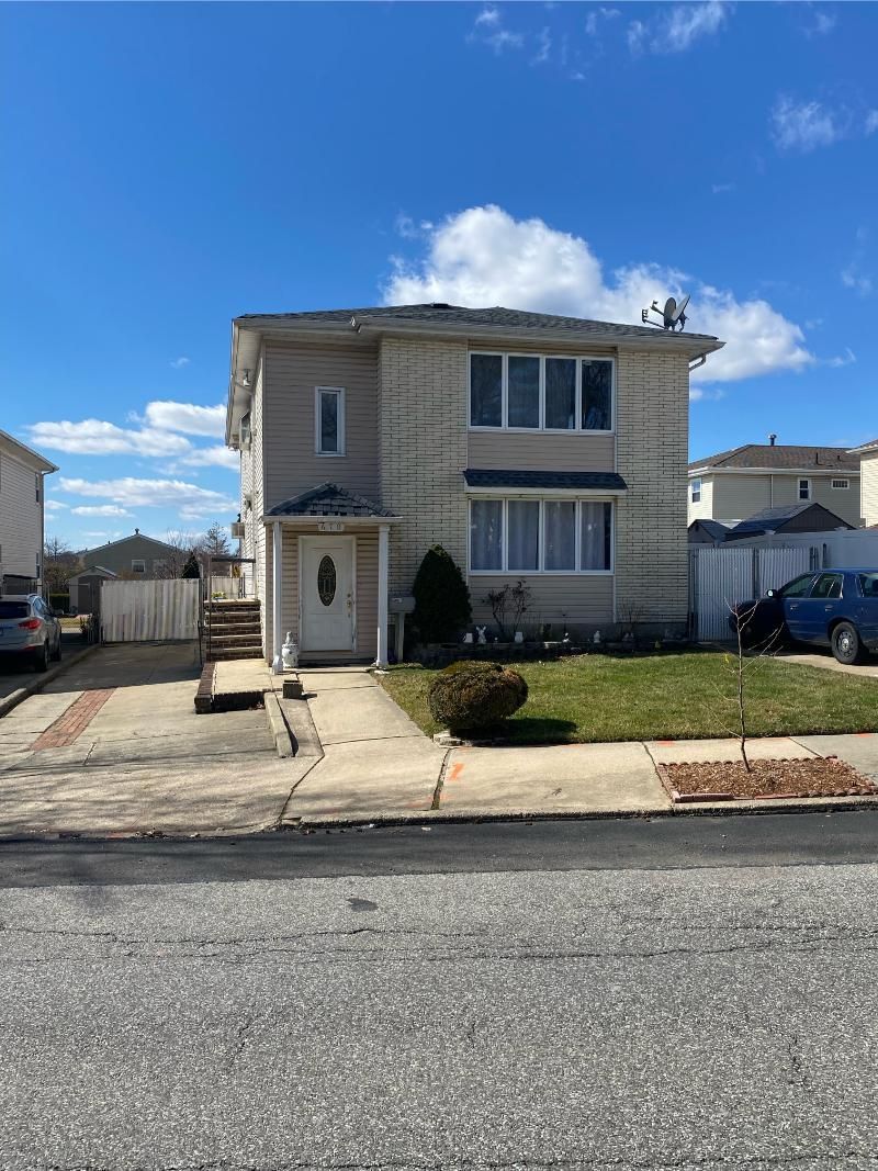 Two-story beige house with white trim, driveway, small lawn, and blue sky on a suburban street.
