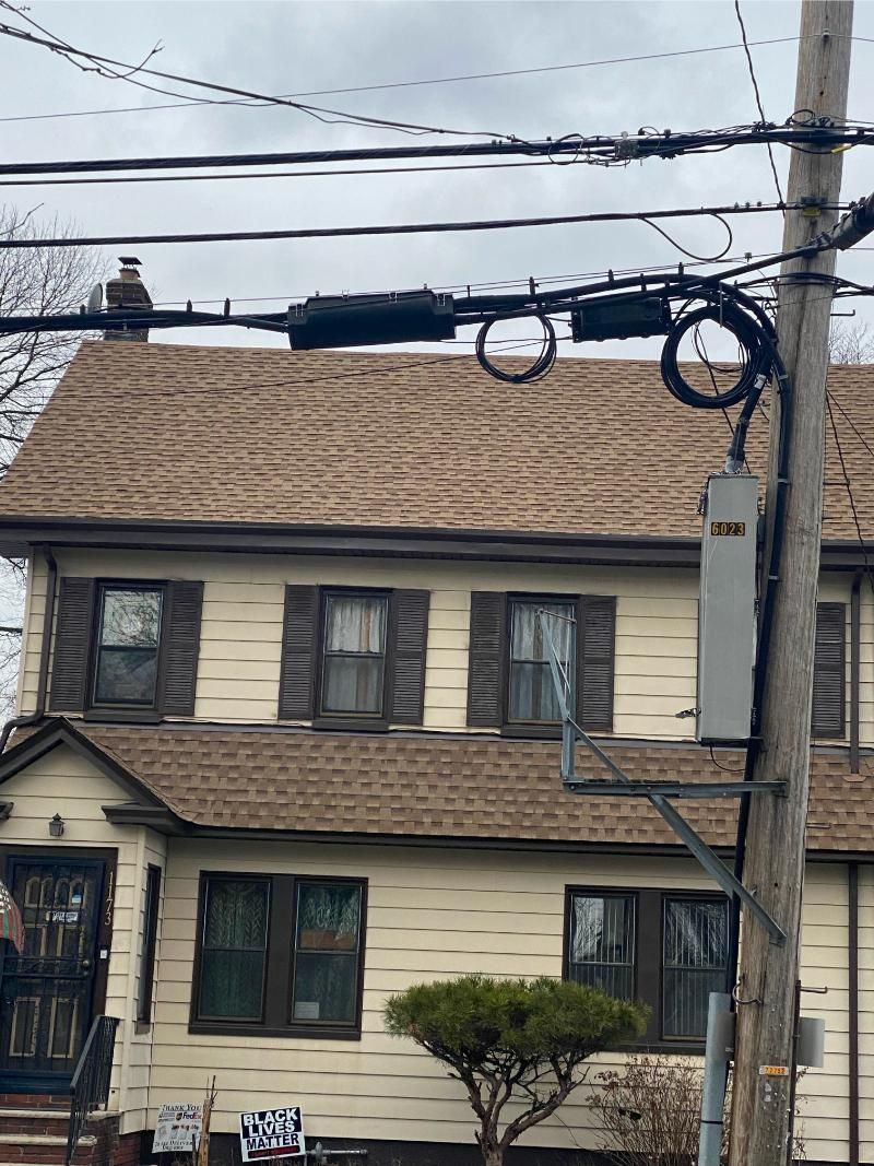 Two-story cream house with brown roof, tree in front, and utility pole with wires overhead
