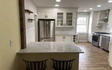 Bright modern kitchen with white cabinets, stainless appliances, island, and two black chairs