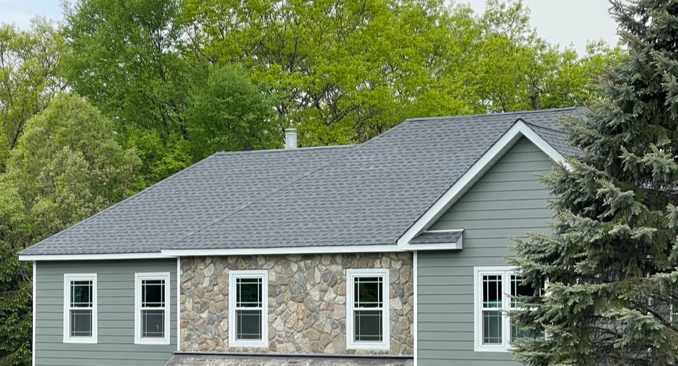 Gray house with stone accents and dark roof, surrounded by green trees