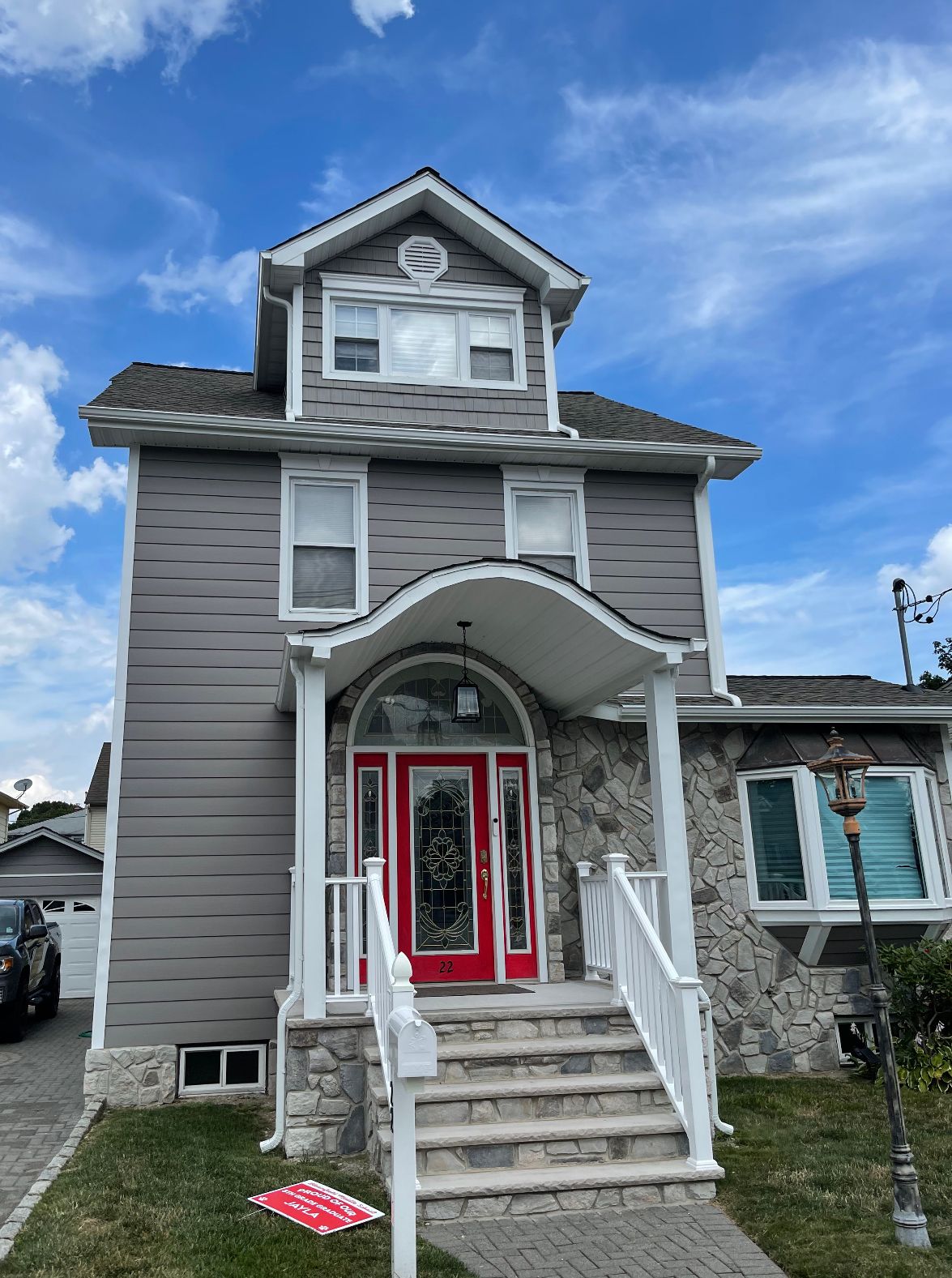 Gray two-story house with red front door, arched porch, and front steps under a blue sky