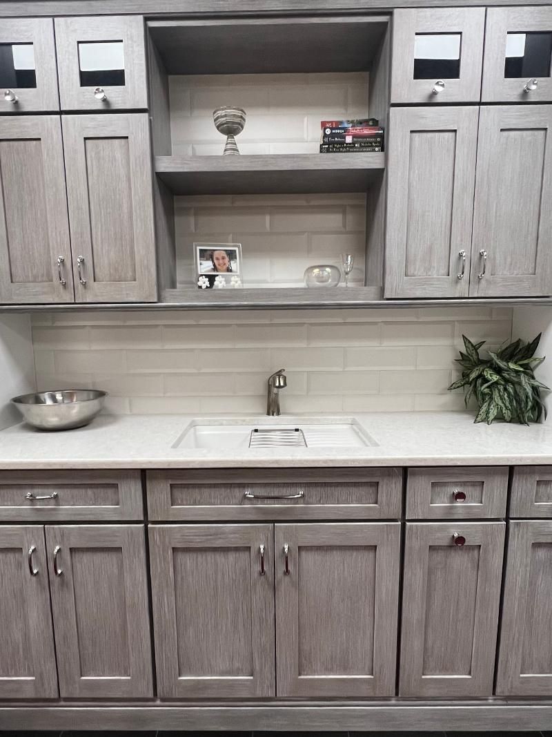 Gray kitchen cabinets and white countertops with open shelving and a sink, neatly styled with decor.