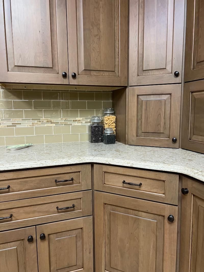 Wooden kitchen cabinets, light granite countertop, and beige tile backsplash with jars on the counter