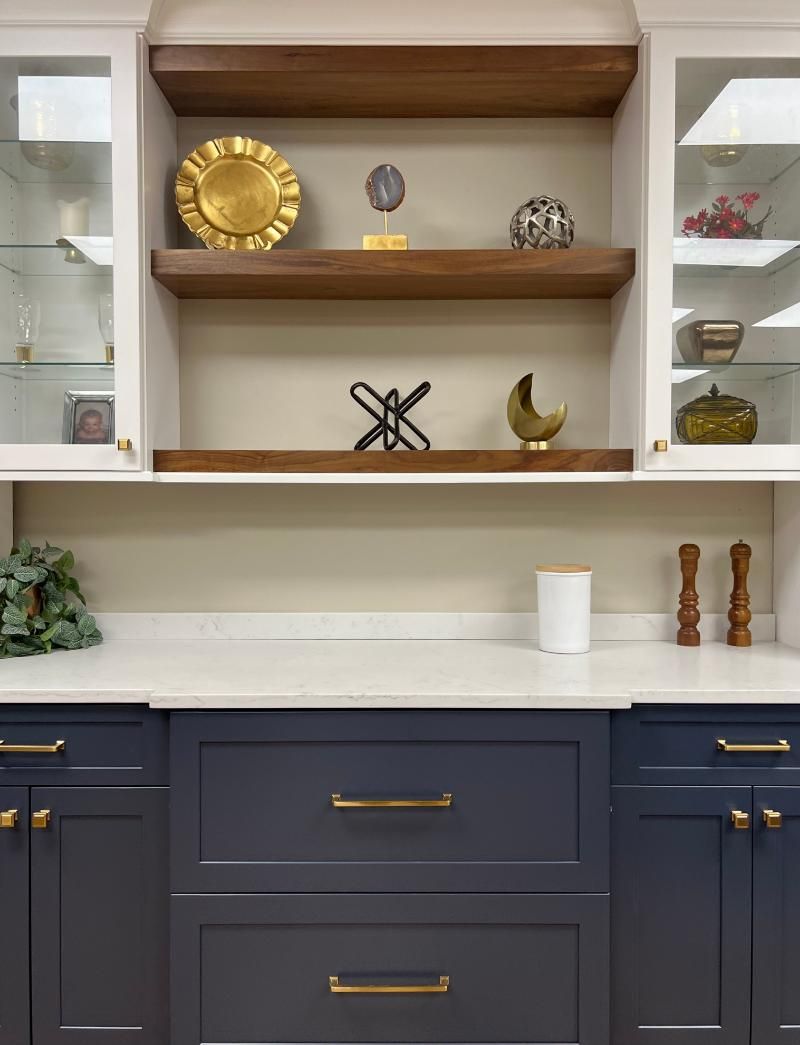 Built-in white shelves with brass decor above a dark blue cabinet and white countertop
