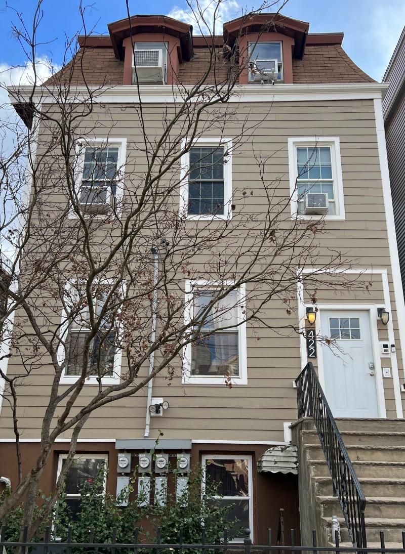 Three-story beige townhouse with white trim, leafless trees, and front steps leading to a white door