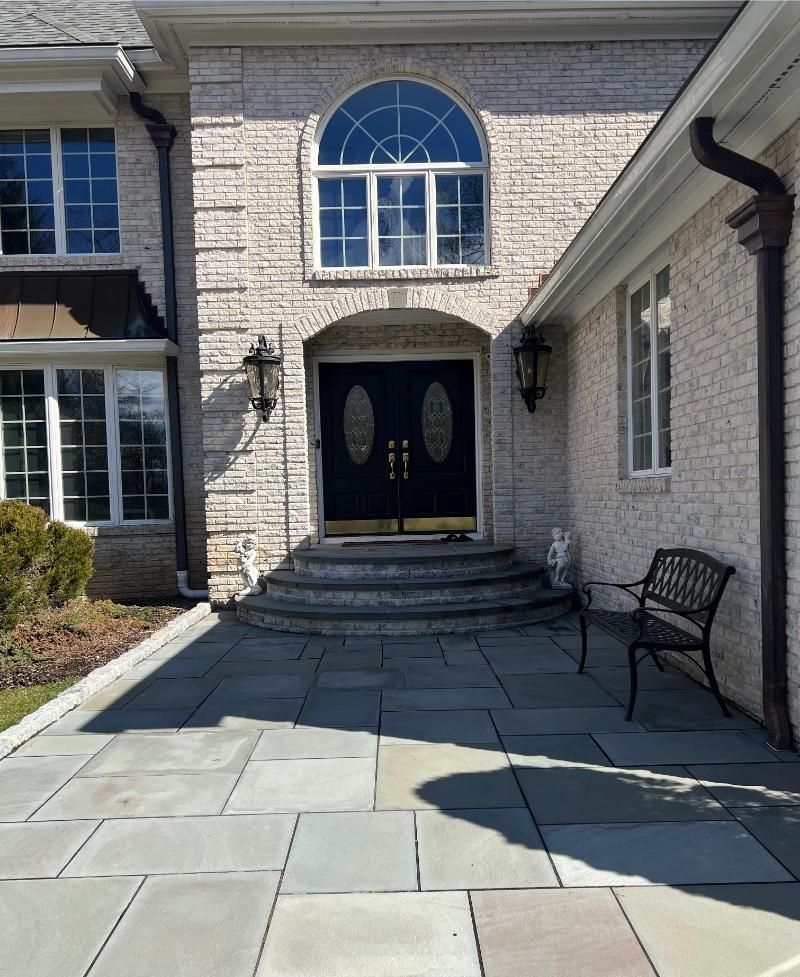 Front walkway to a stone house with double doors, arched window, and a bench by the entrance.