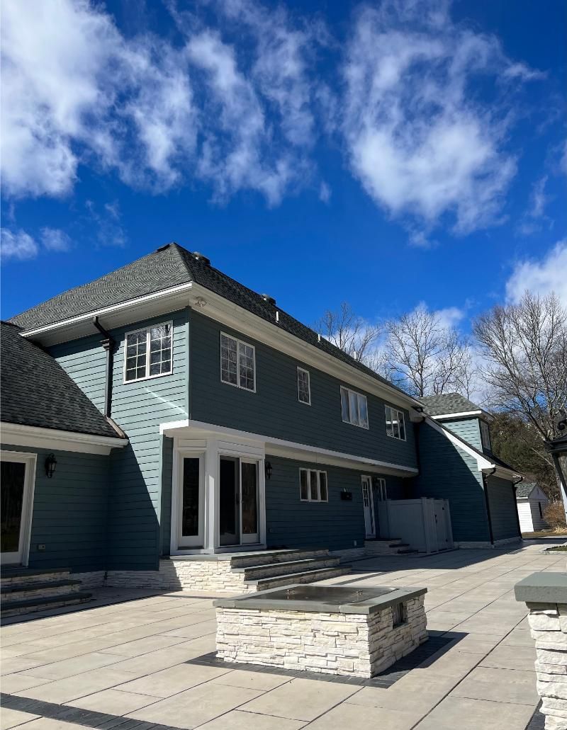 Two-story blue house with white trim and a stone patio under a bright blue sky