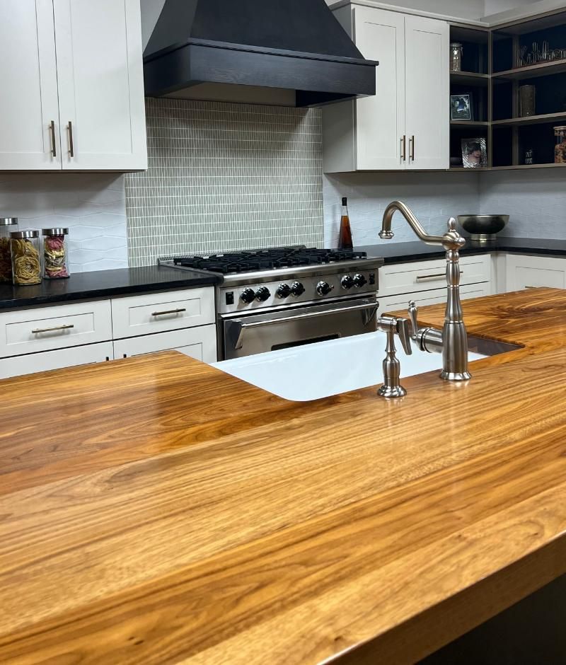Modern kitchen with wood island, stainless steel range, white cabinets, and black backsplash