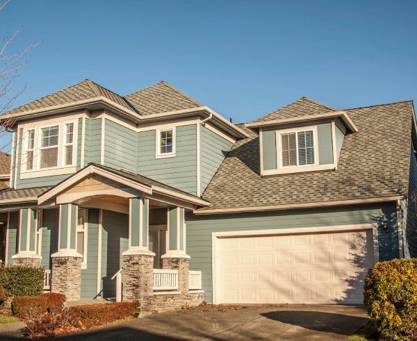 Two-story suburban house with light blue siding, beige trim, and a tan garage under a clear sky