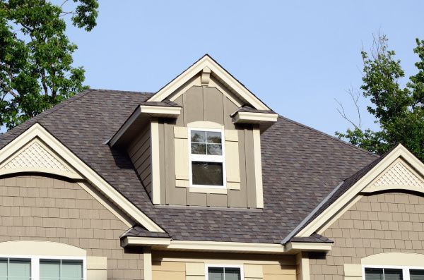 Dormer window on a tan house with a dark shingled roof against a blue sky