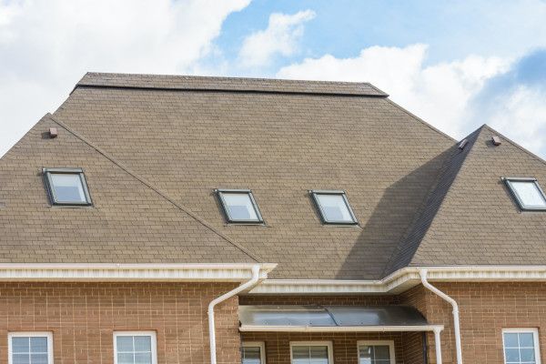 Brick house with a steep gray roof and several skylight windows under a partly cloudy sky