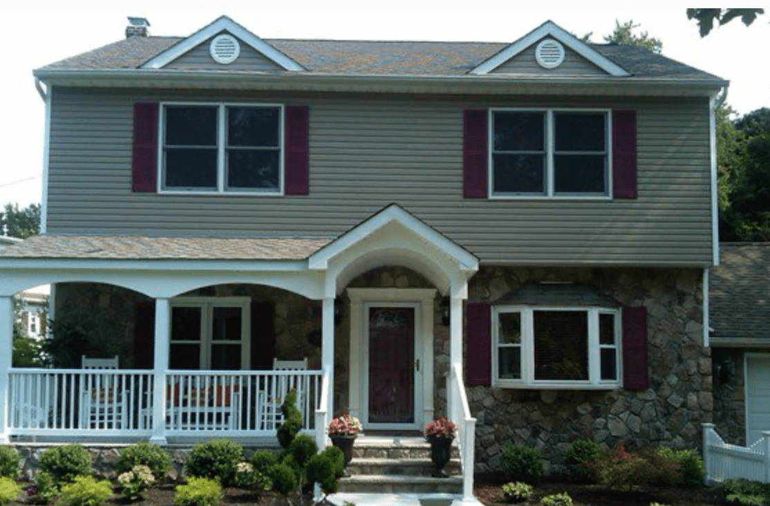 Two-story house with gray siding, stone facade, white porch, and dark red shutters