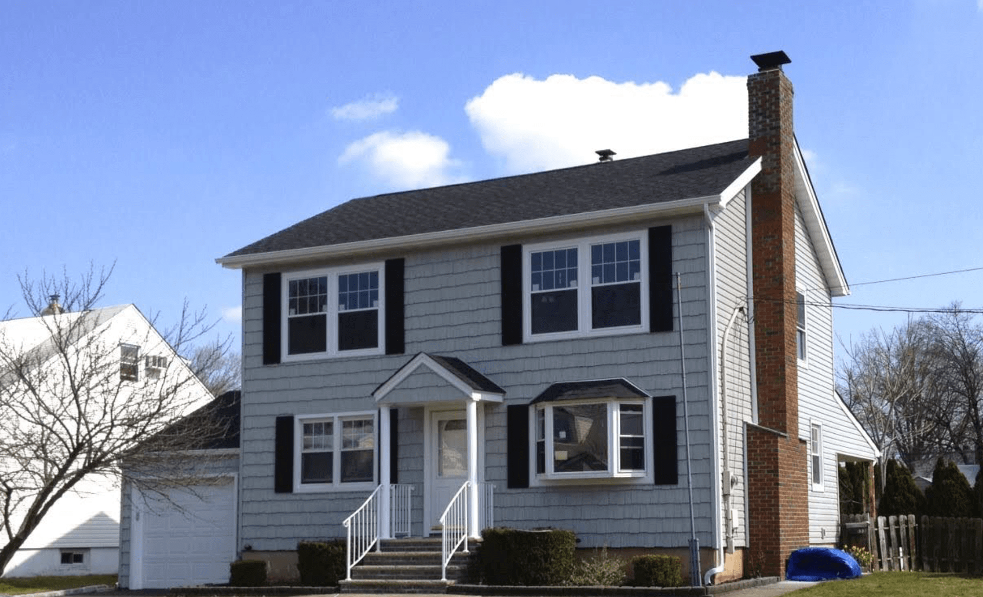 Two-story white house with dark shutters, front porch, and chimney on a sunny day