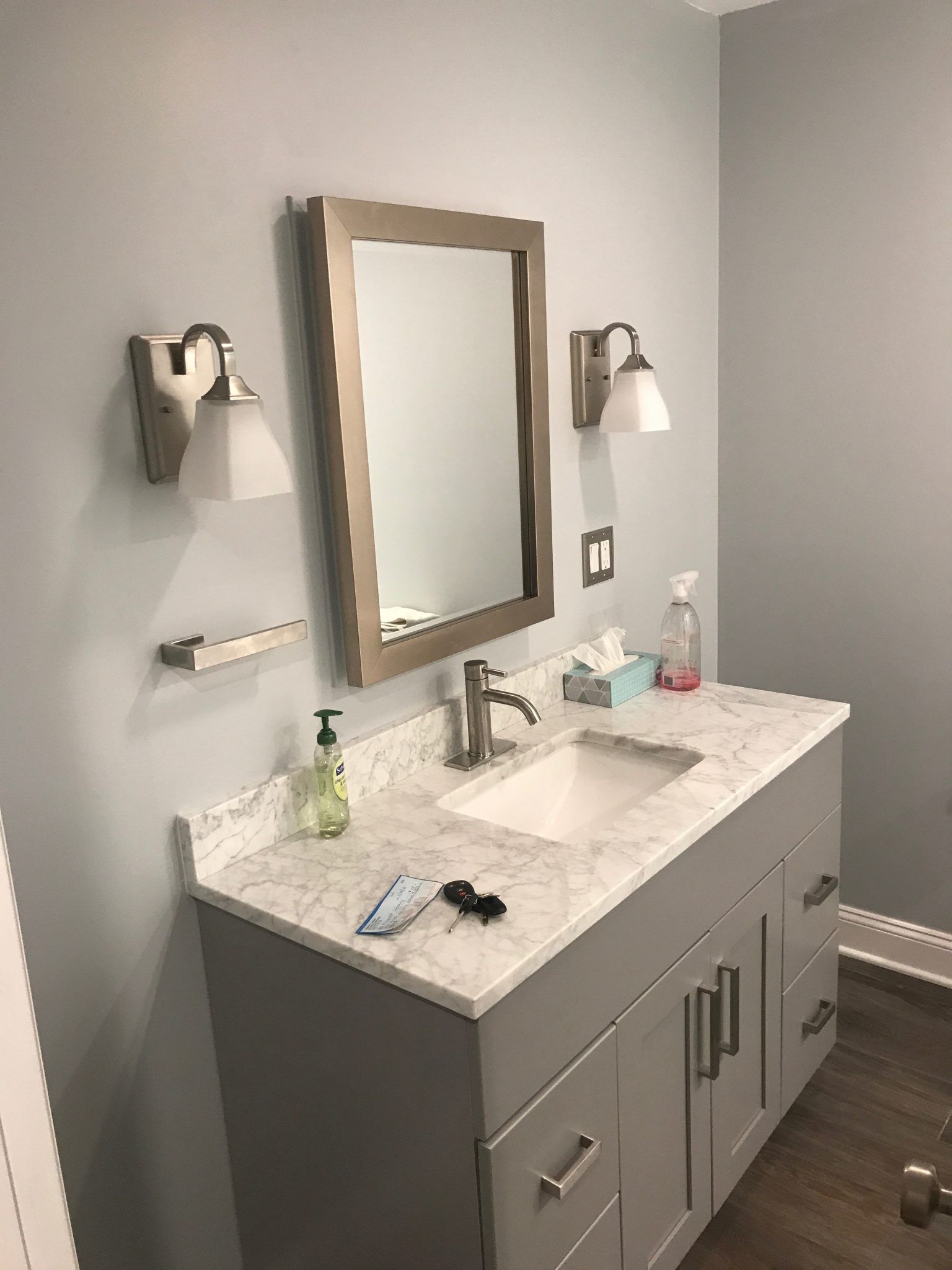 Modern bathroom vanity with double sink, gray cabinets, mirror, wall sconces, and marble countertop