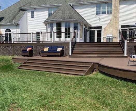 Backyard deck with wide wooden steps, railings, and two lounge chairs in front of a house