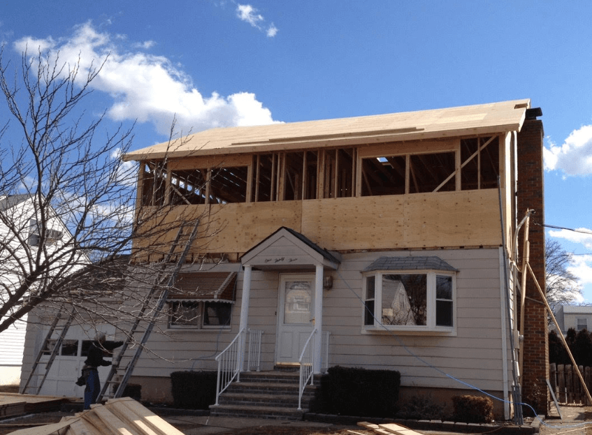 Partially renovated two-story house with exposed upper framing and snow on the ground under a blue sky