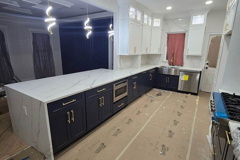 Large unfinished kitchen with dark lower cabinets, white upper cabinets, and a long island under exposed lights.