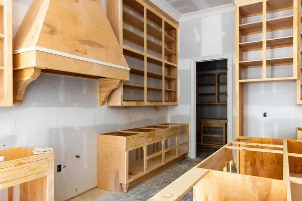 Unfinished kitchen with light wood cabinets, open shelving, and a large range hood under installation