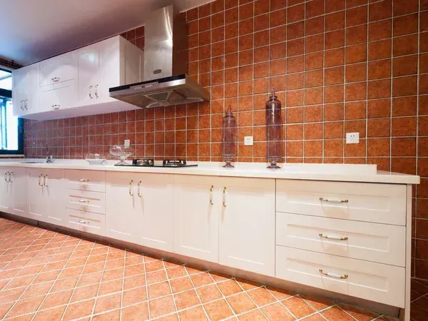 Modern kitchen with white cabinets, orange tile backsplash, stainless range hood, and matching tiled floor