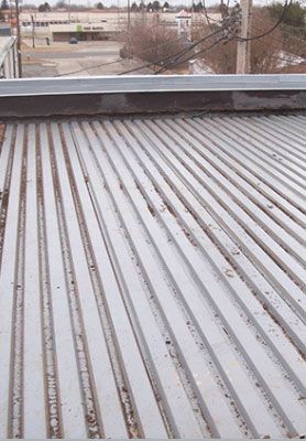 Corrugated metal roof with snow and a distant industrial yard under a gray sky